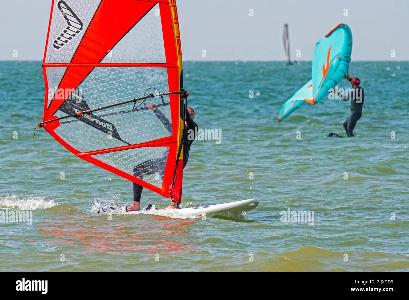 Mädchen / weibliche Freizeit Windsurfer in schwarzem Neoprenanzug üben klassischen Windsurfen und Wingboarder / Wing Boarder Flügel foiling auf See Stockfoto