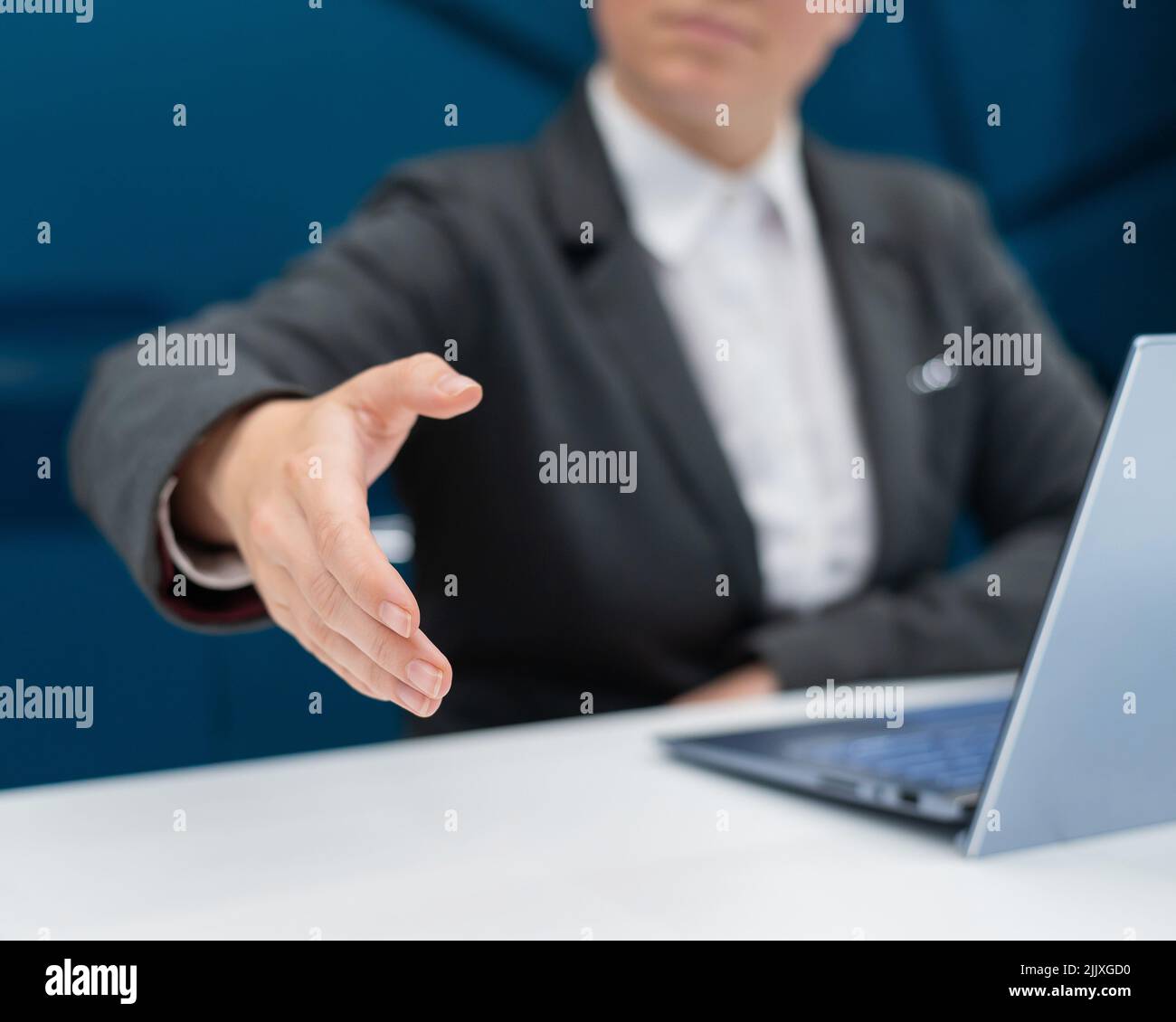 Gesichtslose Frau in einem Business-Anzug streut ihre Hand zum Händeschütteln, während sie an einem Schreibtisch sitzt. Weibliche Chefin macht einen erfolgreichen Deal. Stockfoto