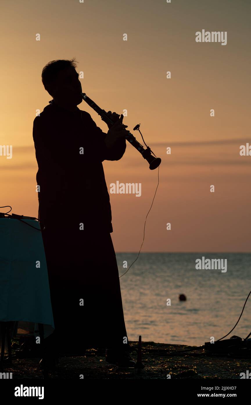 Musiker in Silhouette spielt Instrumente bei Sonnenaufgang am Meer Stockfoto