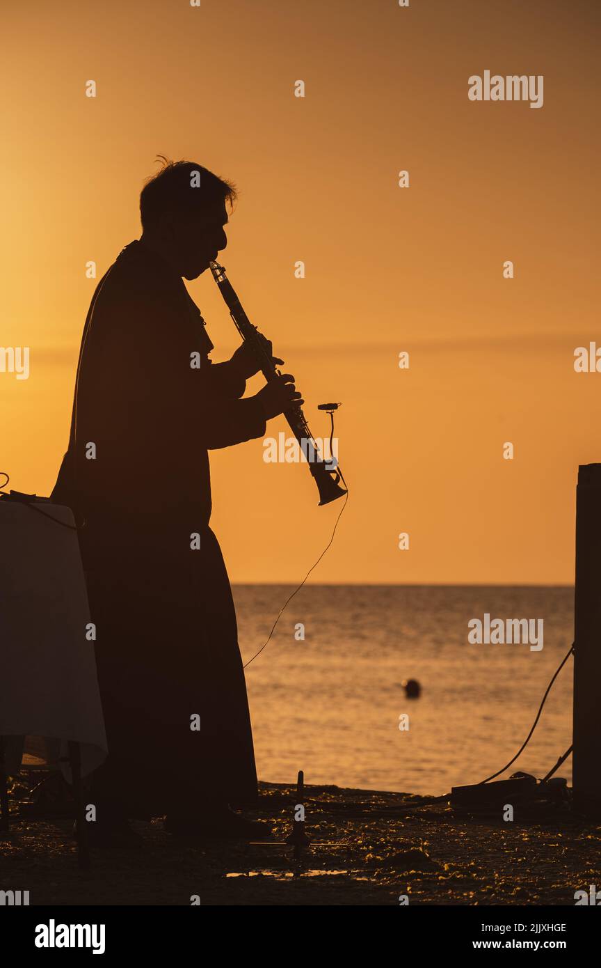 Musiker in Silhouette spielt Instrumente bei Sonnenaufgang am Meer Stockfoto