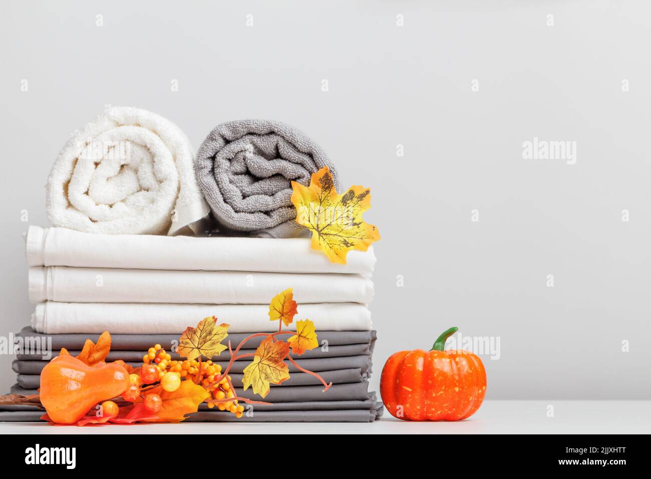 Weiße und graue Bettwäsche, Bettwäsche und zwei gefaltete Handtücher auf einem Tisch mit halloween-Dekor. Stockfoto