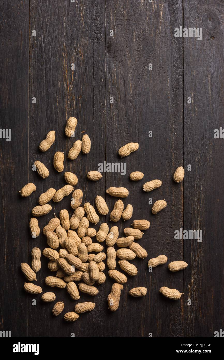 Ungeschälte Erdnüsse, die auf einem dunklen Holzhintergrund verstreut sind, auch als Erdnuss, Gänseleber, pindar oder Affenmutter bekannt, direkt von oben entnommen Stockfoto
