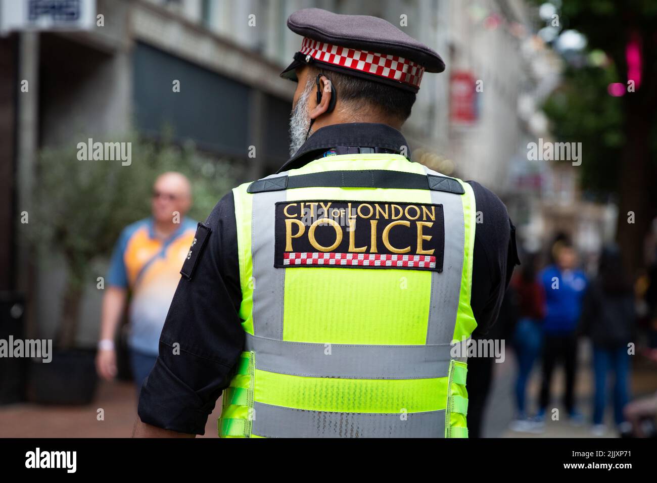 LONDON, GROSSBRITANNIEN - 28. JULI 2022. Eine Rückansicht eines Metropolitan-Polizisten in Uniform und auf der Straße mit einem City of London Polizeischild auf seinem Rücken Stockfoto