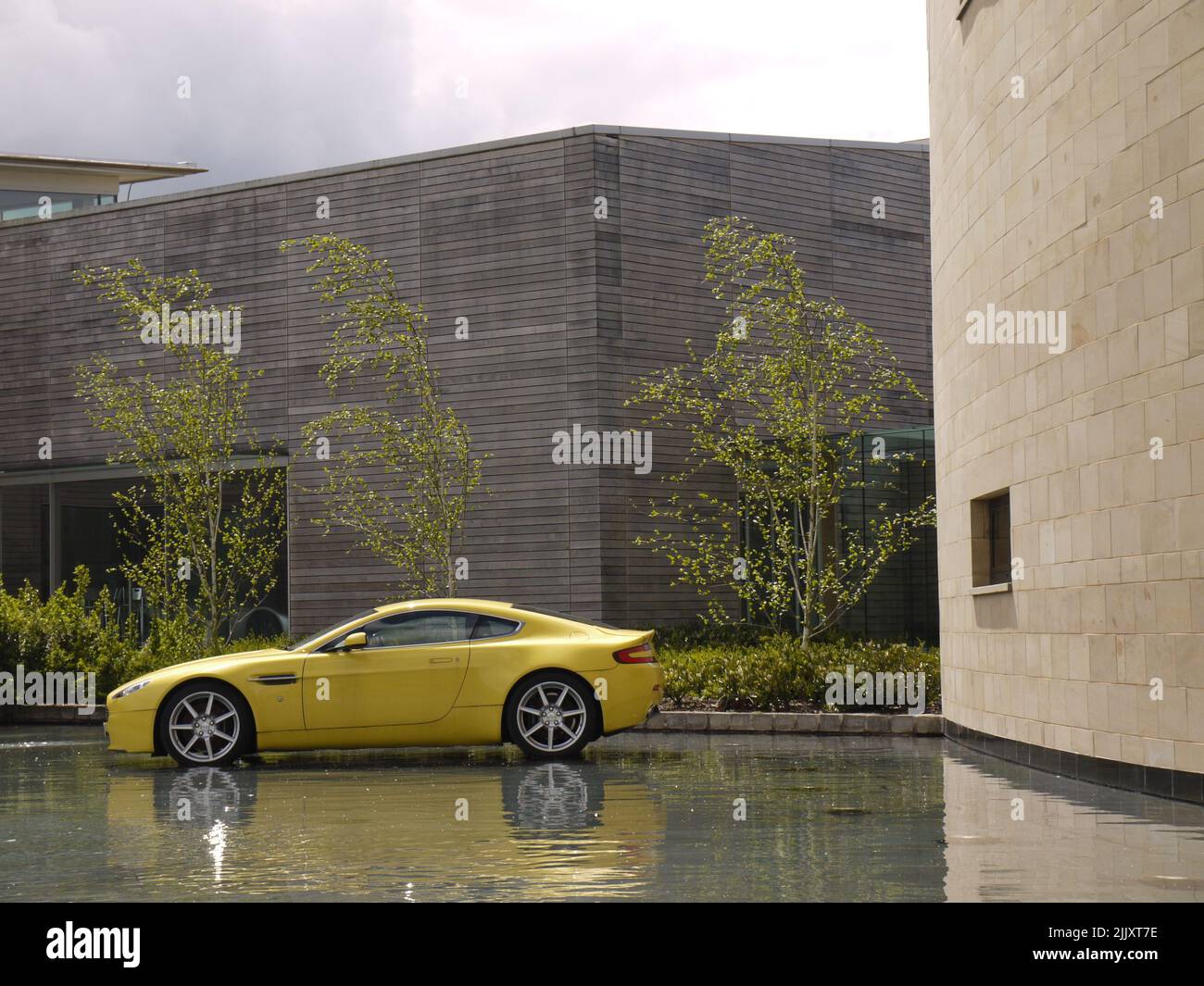 Ein Sunburst Yellow Aston Martin Vantage wurde im Graben vor DEM Hauptquartier in Gaydon, Warwickshire, mit Gaydon Design Studio im Hintergrund angezeigt Stockfoto