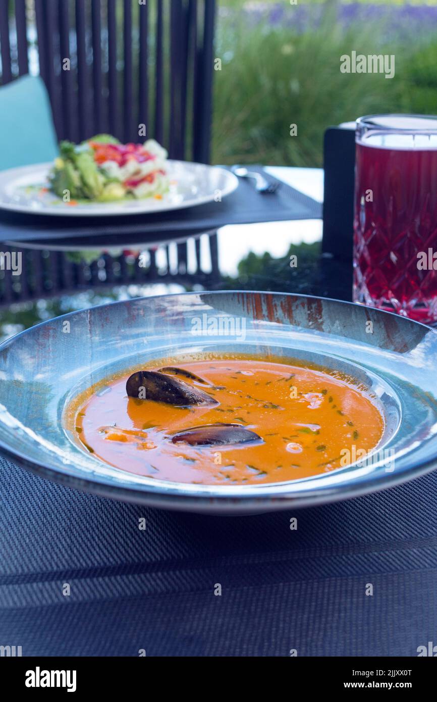 Köstliche Meeresfrüchte Tomatensoße mit Bouillabaisse Fischsuppe mit Garnelen, Muscheln und Fisch auf einem blauen Teller auf dem Tisch. Köstliches romantisches Abendessen in einer Fischruhe Stockfoto
