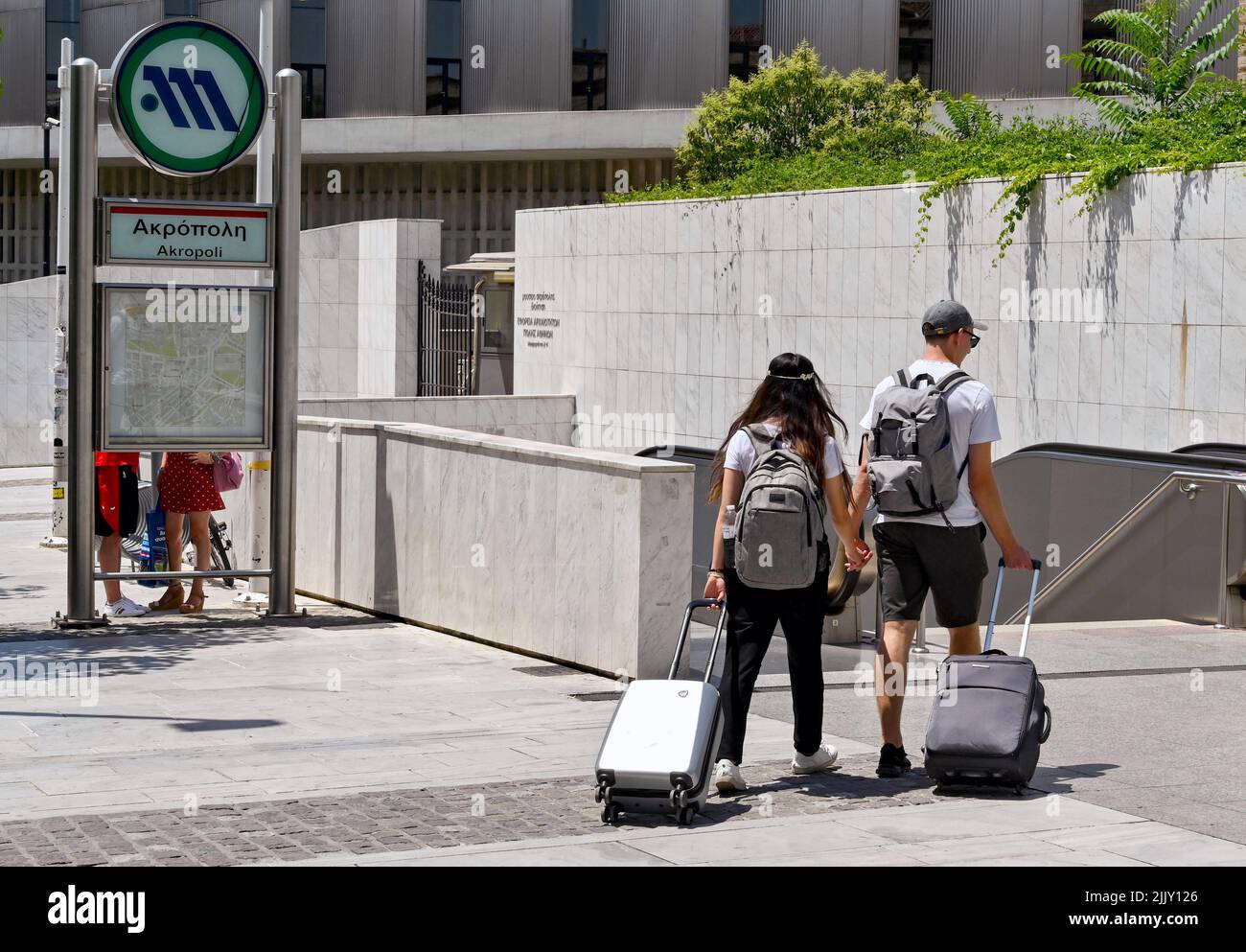Athen, Griechenland - 2022. Juni: Zwei junge Menschen mit Gepäck gehen Hand in Hand in den Eingang der Metro-Station der Stadt an der Akropolis. Stockfoto