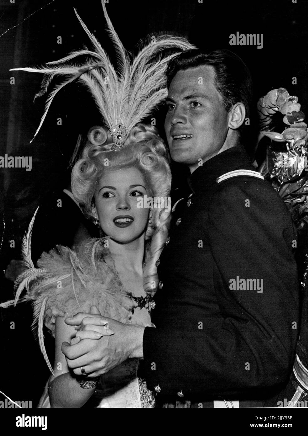 Shirley Temple tanzt in Federn, während Ehemann John Agar in der Uniform erscheint, die er in RKO's kommendem Fort Apache auf einer kürzlich stattfindenden Party in schicken Kleidern trägt. 19. Dezember 1948. Stockfoto