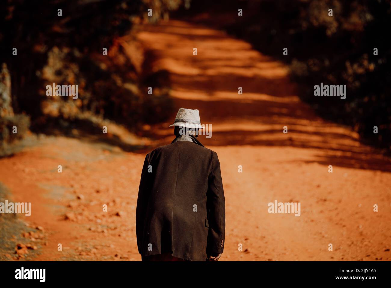 Ein alter Mann geht entlang der roten Straßen Afrikas. Illustratives Foto des Lebens in Afrika und Kenia. Leben eines Rentners im Ruhestand in Ostafrika Stockfoto