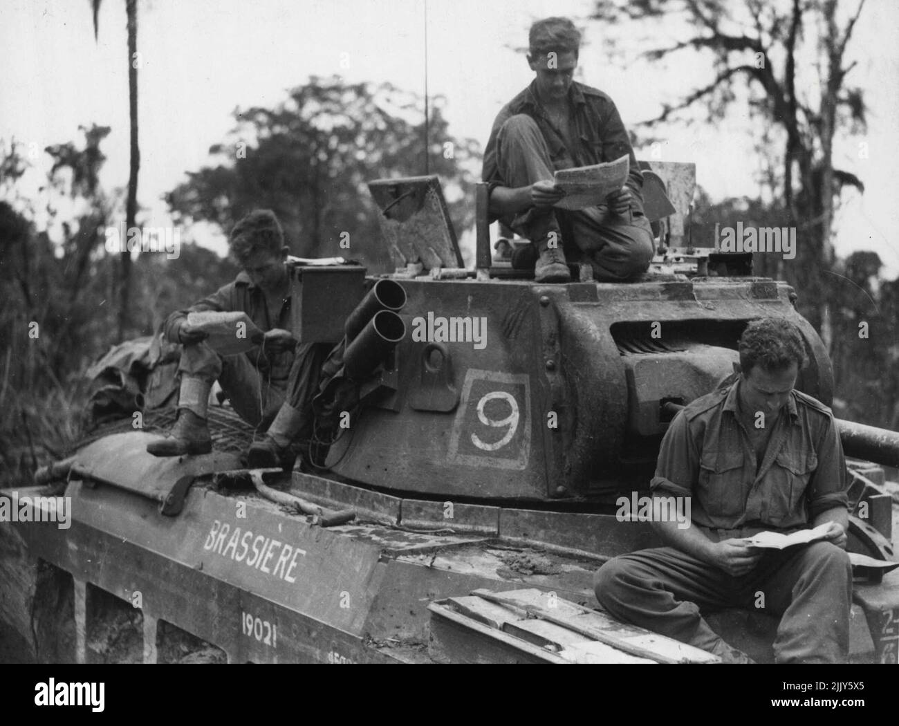 Mitglieder einer australischen Panzerbesatzung lasen Post, während sie auf Befehle warteten, sich zur Unterstützung von 3. zu bewegen. Division-Infanterie. Auf Bougainville. 5. Juni 1945. (Foto von Australian Official Photo). Stockfoto