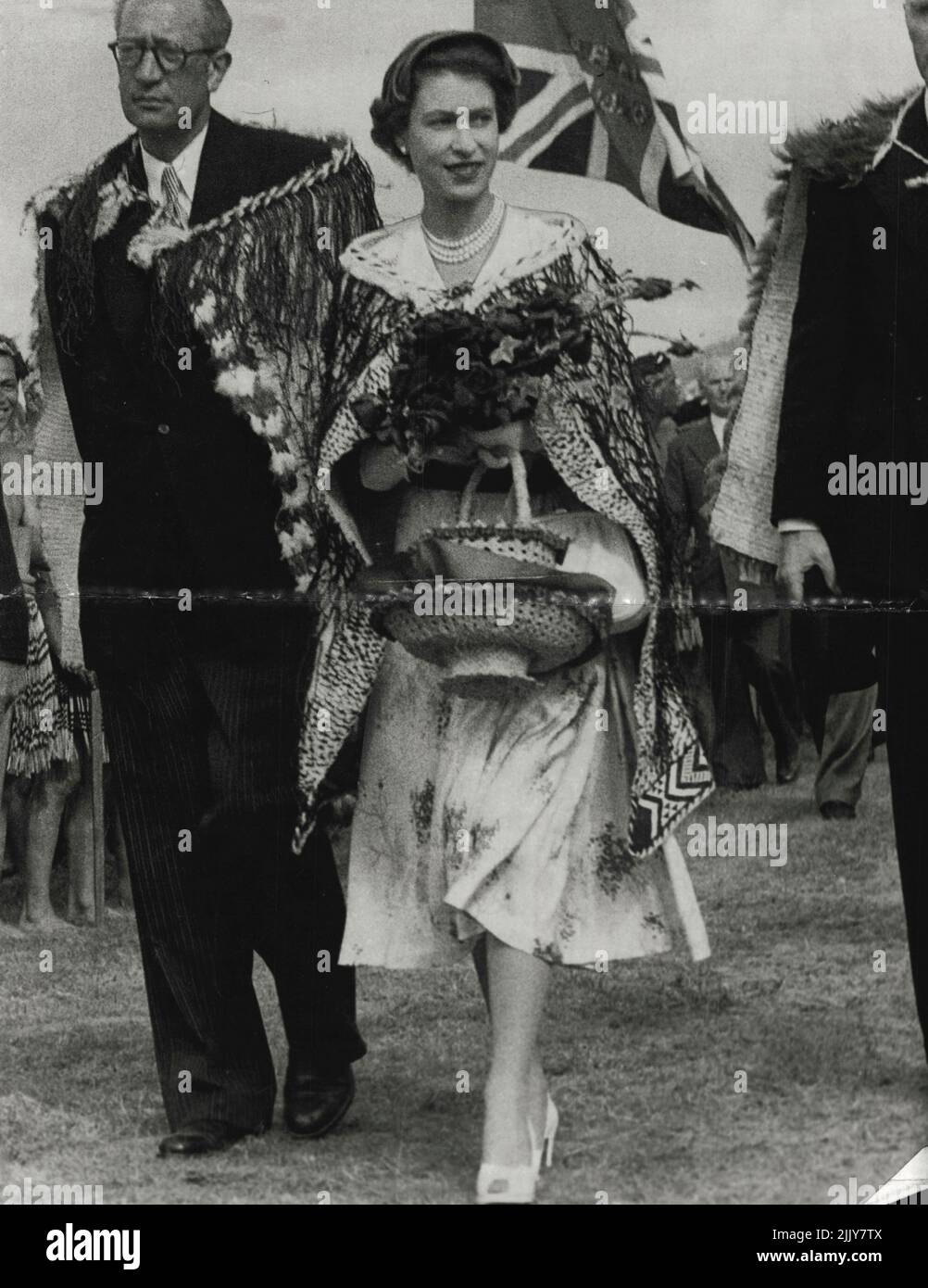 Geschenke - Queen Elizabeth ***** Charmant und glücklich, als sie im Mantel eines Maori-Chefs eine Maroi-Zeremonie im Arawa Park, Rotorua, verlässt. Die Königin trägt Geschenke von Blumen und zwei Körbe. 07. Januar 1954. Stockfoto