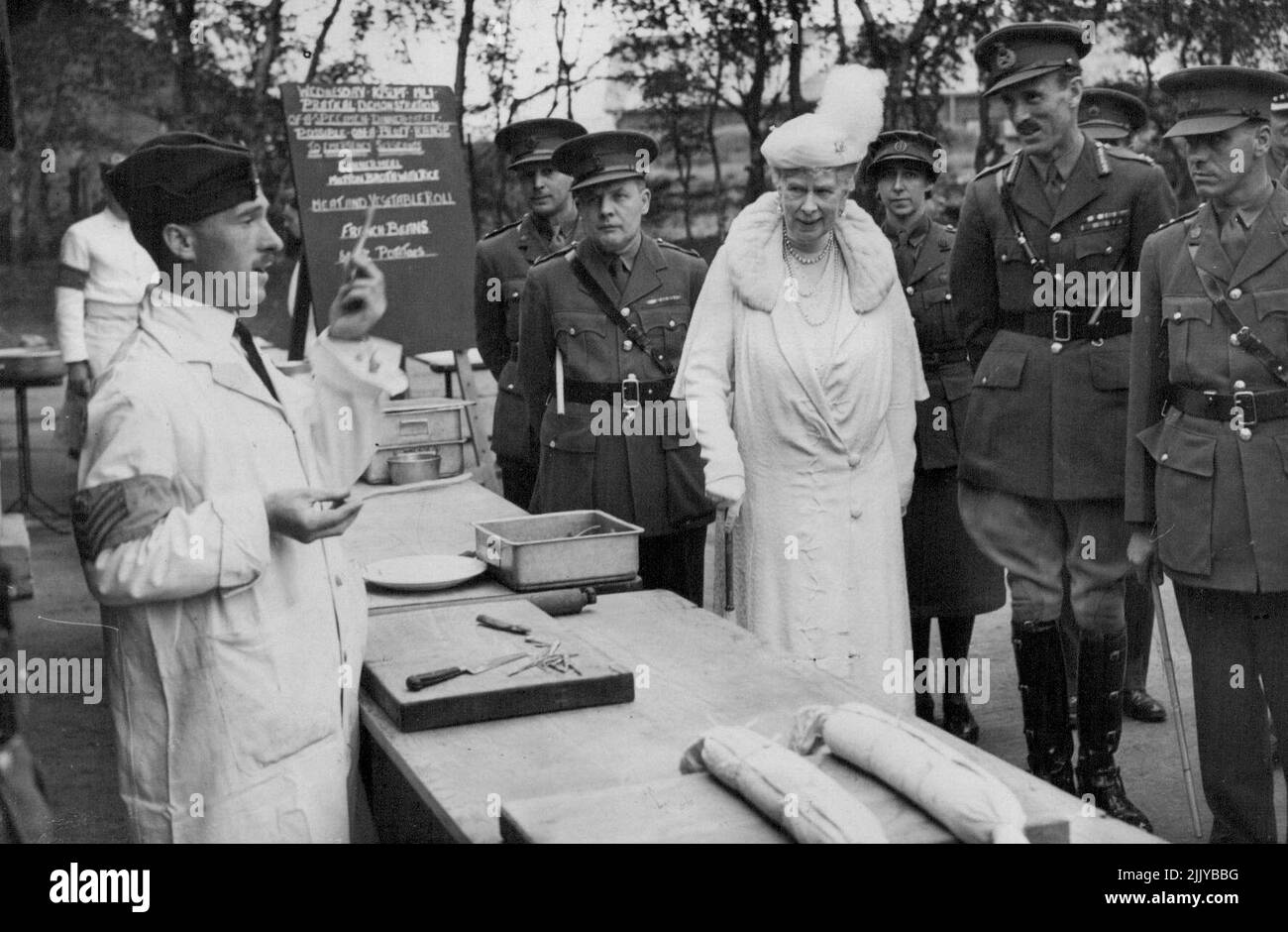 Queen Mary Besucht Armeestützhäuser In Südengland. -- Königin Mary bleibt, um zuzuhören, während ein Sergeant Instructor während ihres Besuchs in der Army School of Cookery einen Vortrag über das Kochen von Läuferbohnen hält. Queen Mary besuchte verschiedene Armeestützhäuser in Südengland umfassend, inspizierte die Armeeschule für Kochkunst, besuchte ein Heim für Kinder von Soldatenfamilien und nahm den Gruß an einem marsch an einem Ontario-Regiment, dessen Oberst sie ist, Teil. 12. September 1941. Stockfoto
