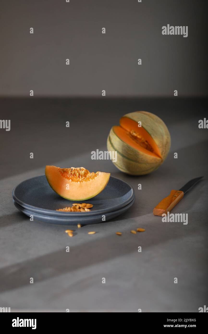 Scheibe Melone, Honigmelone auf grauem Teller. Melone, Messer auf grauem Hintergrund. Obst. Gesundes Lebensmittelkonzept. Stockfoto