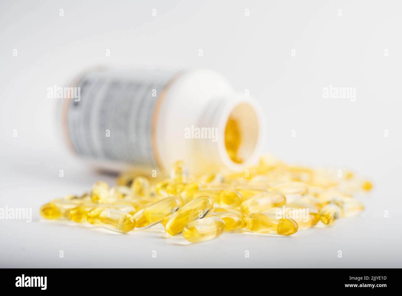 Gelbe Fischöl-Kapseln in einer Gelee-Schale in der Nähe des weißen Glases. Vitamine und Diätpillen Ergänzungen. Gesundheitskonzept Stockfoto