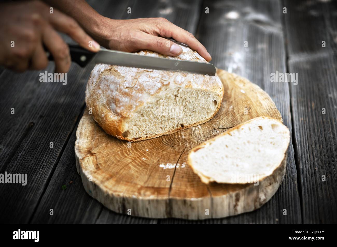 Traditionelles Sauerteig-Brot, das auf einem rustikalen Holztisch in Scheiben geschnitten wird. Fotos von gesunden Lebensmitteln Stockfoto