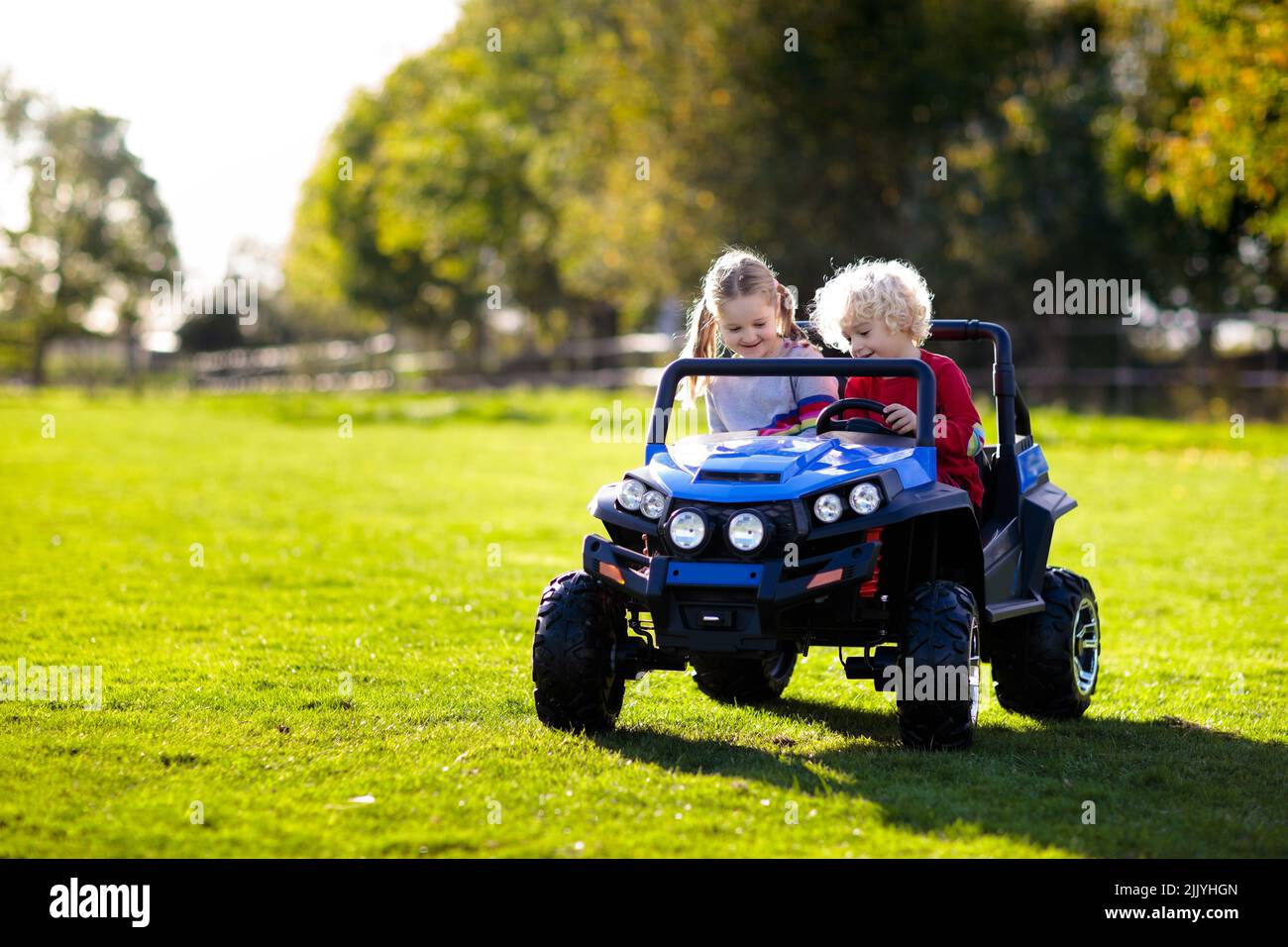 Kinder fahren elektrisch Spielzeugauto im Sommer Park. Outdoor Spielzeug.  Kinder Akku Fahrzeug. Kleine Jungen und Mädchen reiten Spielzeug-LKW im  Garten. Fam Stockfotografie - Alamy