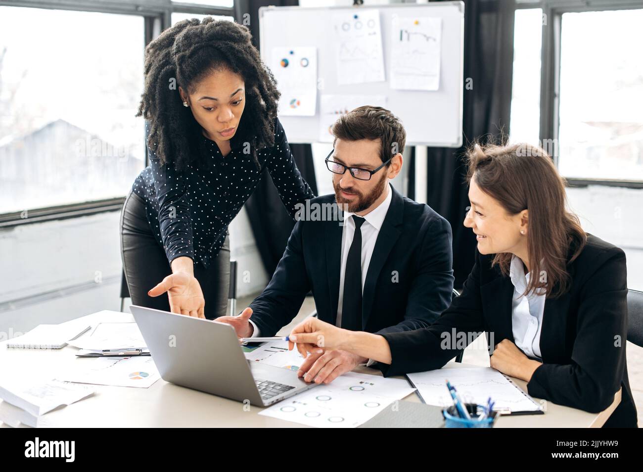 Teamzusammenarbeit von Geschäftsleuten. Multirassische erfolgreiche Kollegen denken gemeinsam an Strategien, sitzen im modernen Kreativbüro, studieren Dokumente, benutzen Laptops, diskutieren Stockfoto