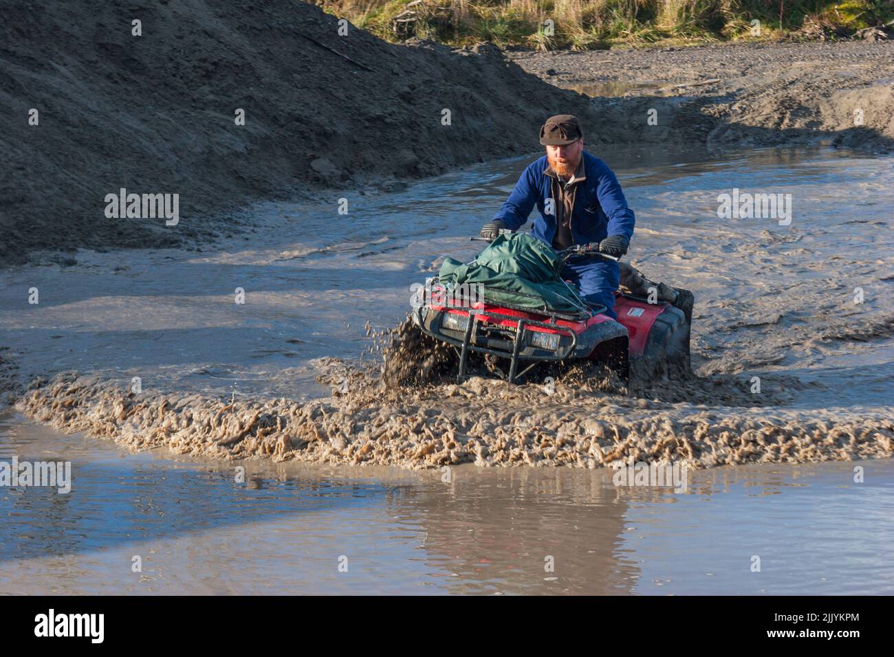 Ein Blick auf das Leben in Neuseeland: Quadbike-Abenteuer den Fluss hinauf. Viel Wasser und Schlamm und herausfordernde Flussüberquerungen. Stockfoto