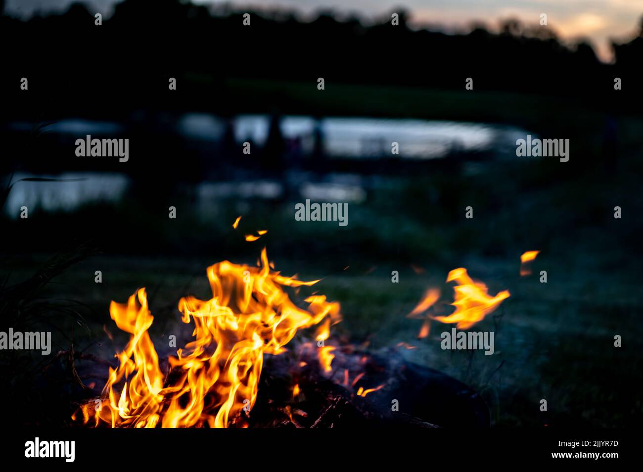 Springende Flammen eines Lagerfeuers mit einem verdunkelten Blick auf einen Teich im Hintergrund. Stockfoto