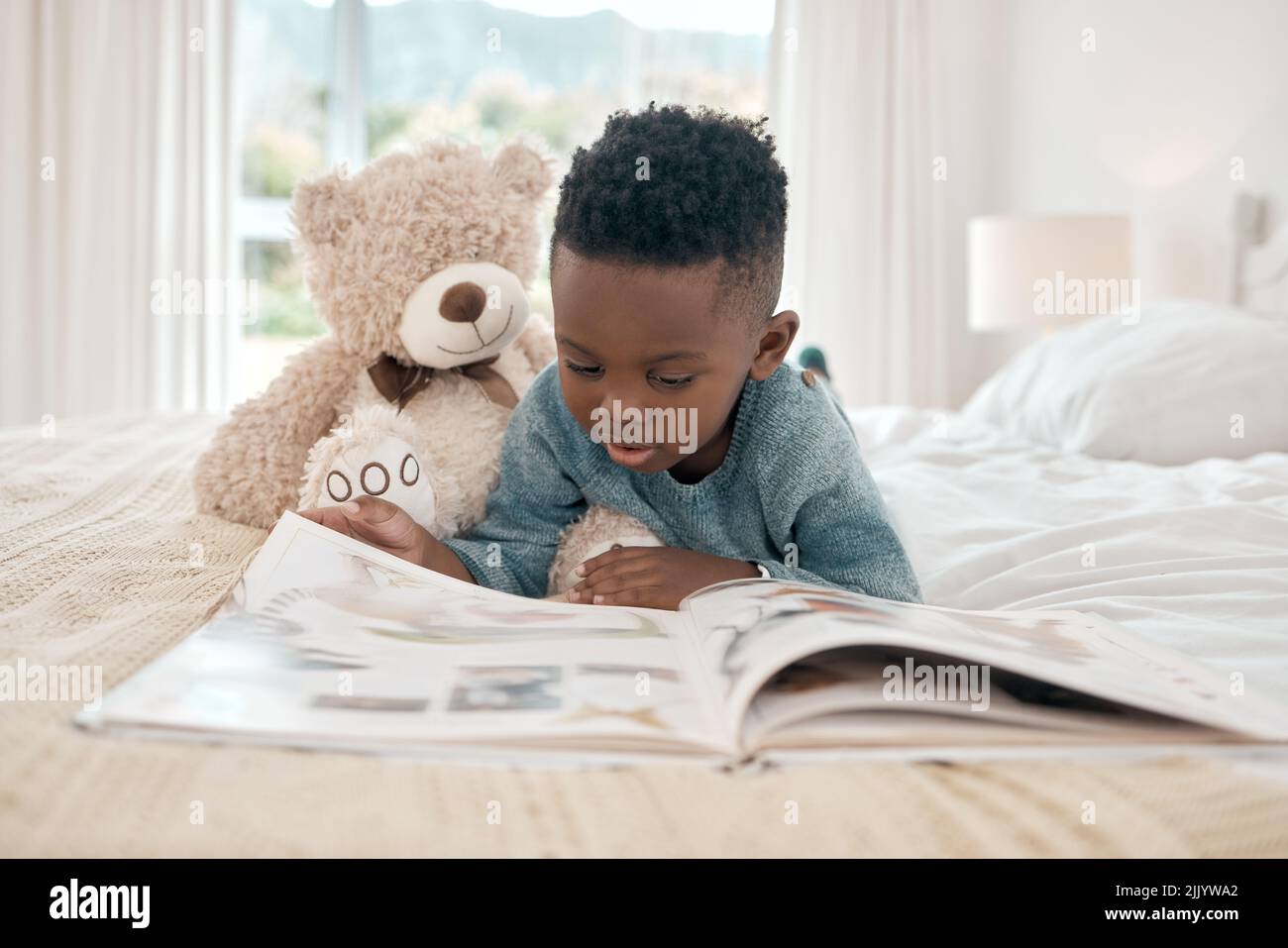 Erweitert seine Vorstellungskraft. Die ganze Aufnahme eines entzückenden kleinen Jungen, der zu Hause ein Buch auf einem Bett liest. Stockfoto