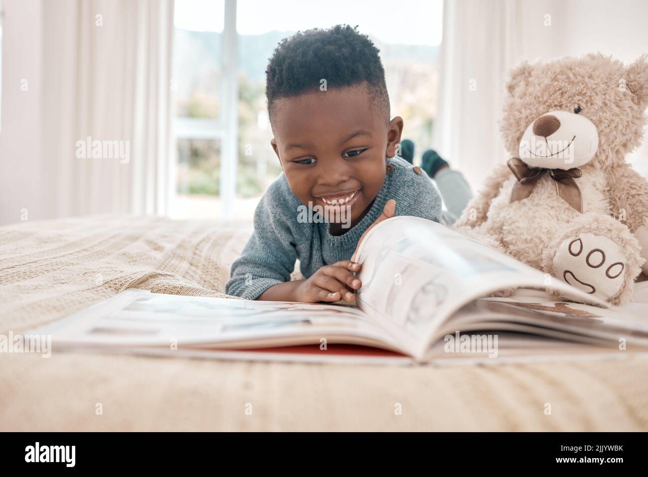 Lesen begeistert ihn. Die ganze Aufnahme eines entzückenden kleinen Jungen, der zu Hause ein Buch auf einem Bett liest. Stockfoto