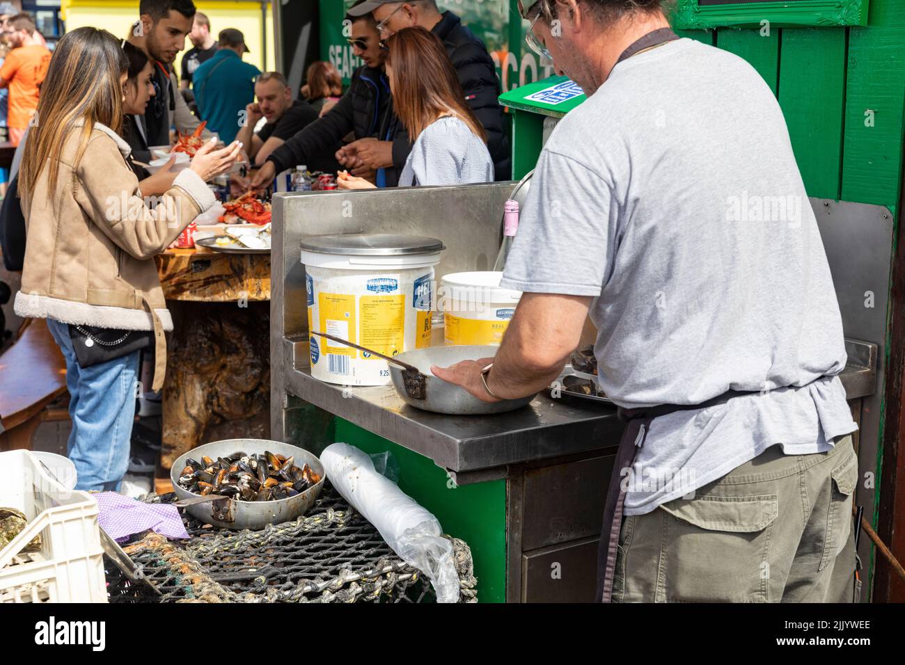 Kunden, die frische Meeresfrüchte und Schalentiere im Hafen von Oban kaufen, Muscheln, Krabben, Hummer, die alle verkauft werden, und Muscheln, die in Knoblauch, Oban, Highlands, Schottland gekocht werden, Stockfoto