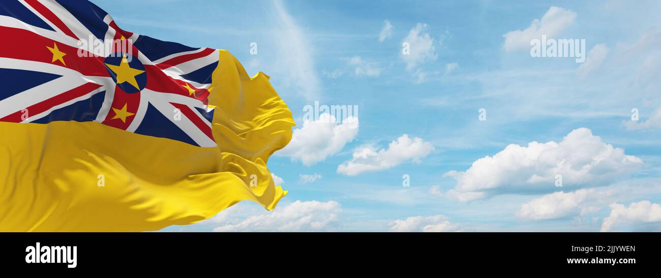 Offizielle Flagge von Niue Neuseeland bei bewölktem Himmel Hintergrund bei Sonnenuntergang, Panoramablick. Neuseeland Reise und patriotische Konzept. Kopieraum für weite Bann Stockfoto