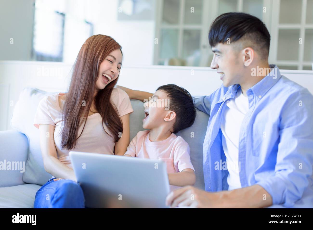 Junge fröhliche Familie, die sich mit dem Laptop auf dem Sofa im Wohnzimmer ausruht Stockfoto