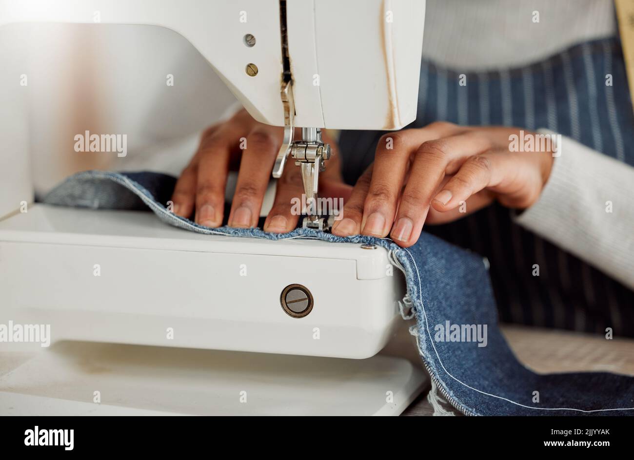 Nahaufnahme einer professionellen Designerin, die in ihrem Atelier auf einer Nähmaschine sitzt. Prozess eines Schneiders bei der Arbeit an Reparatur und Design Stockfoto