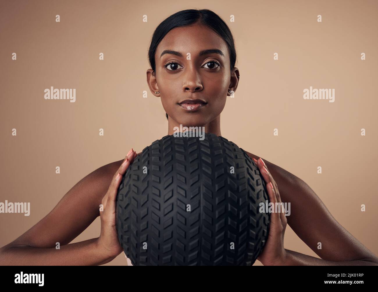 Es ist an der Zeit, die Arme zu straffen. Eine attraktive junge Frau, die allein im Studio steht und beim Arbeiten einen Medizinball hält. Stockfoto