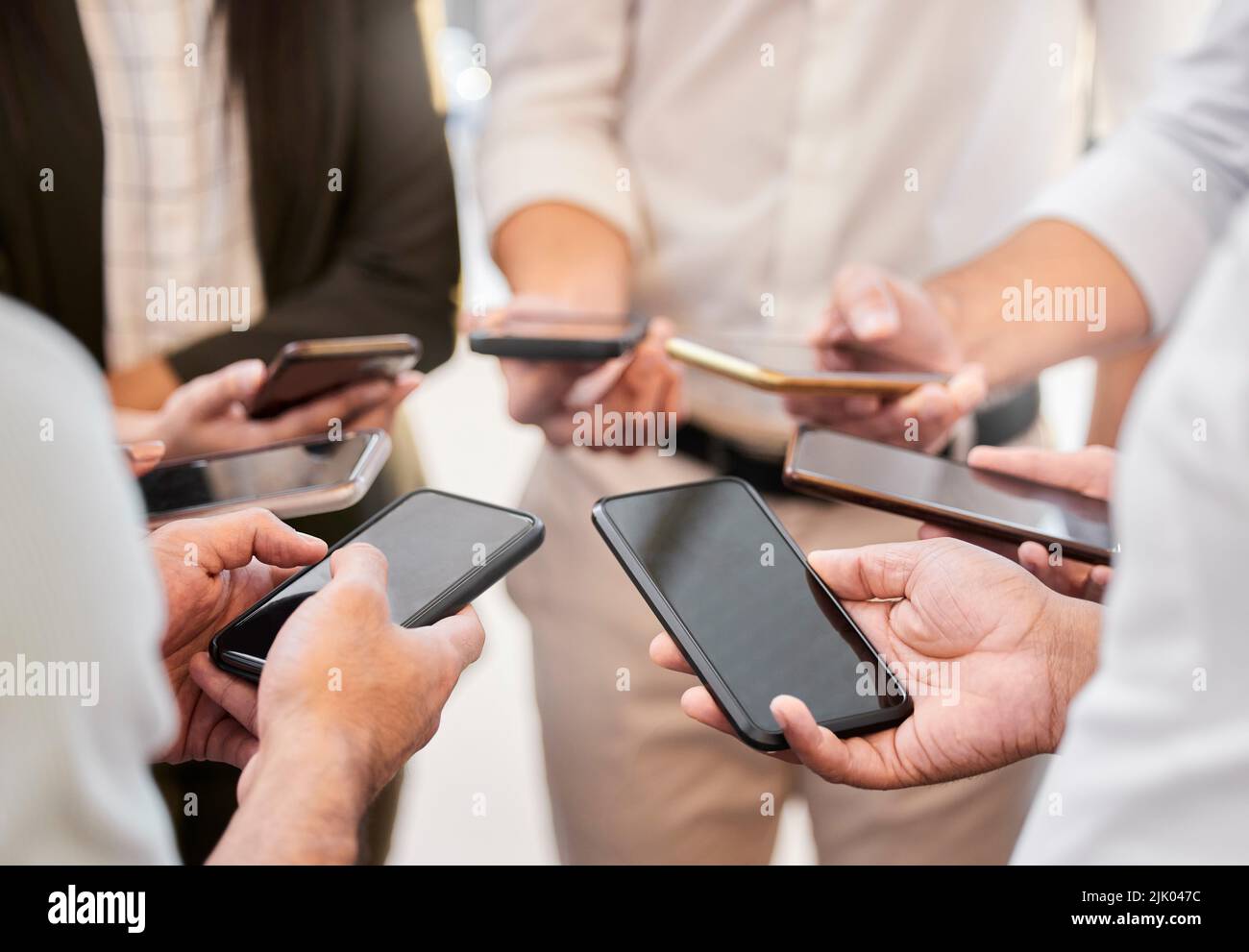 Synchronisierung unserer Zeitpläne. Eine unkenntliche Gruppe von Geschäftsleuten drängte sich im Büro zusammen und benutzte ihre Handys. Stockfoto