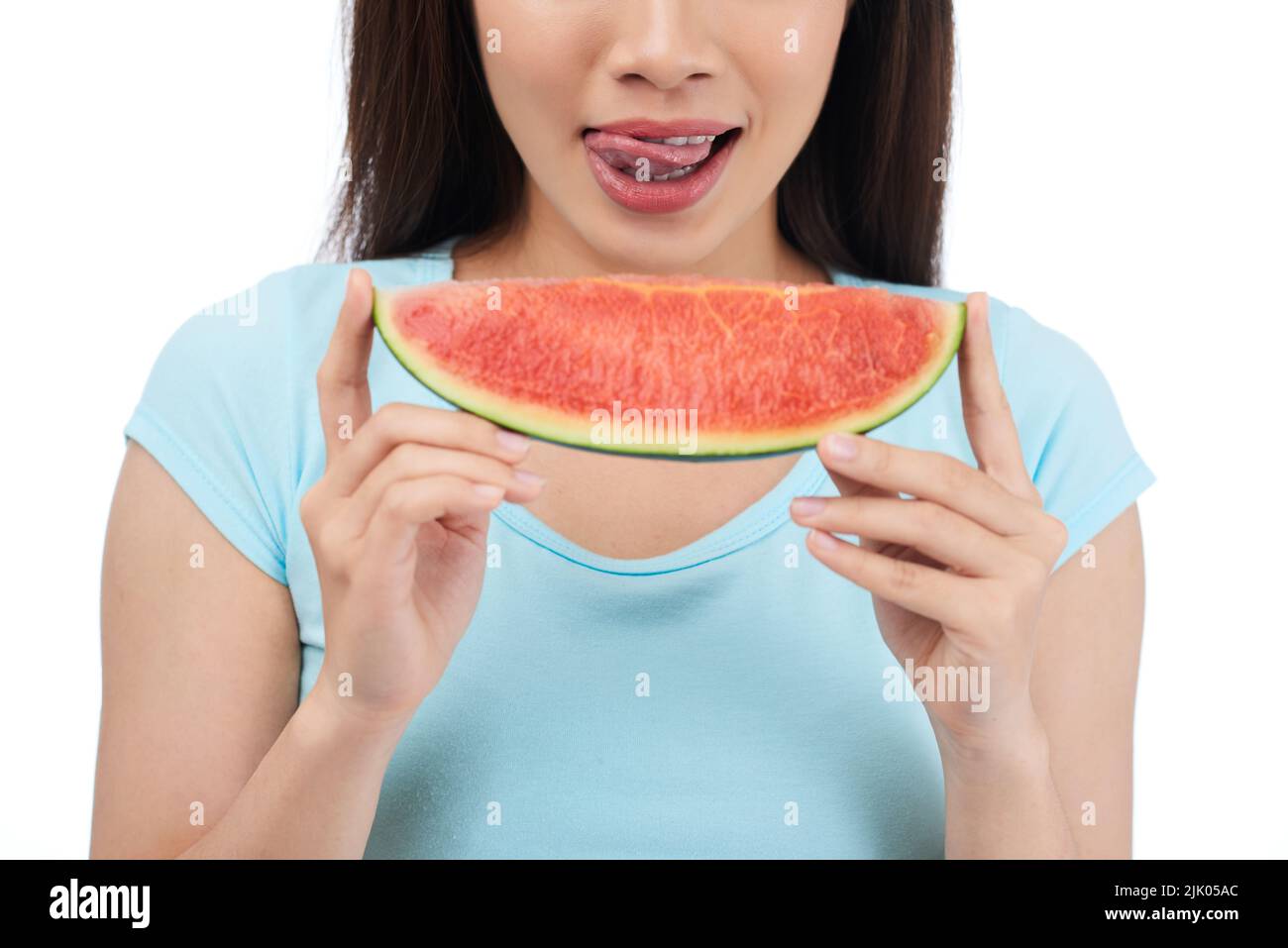 Nahaufnahme einer unkenntlichen Frau, die ihre Lippen leckt, während sie eine saftige Wassermelone in den Händen hält, isoliert auf weißem Hintergrund Stockfoto
