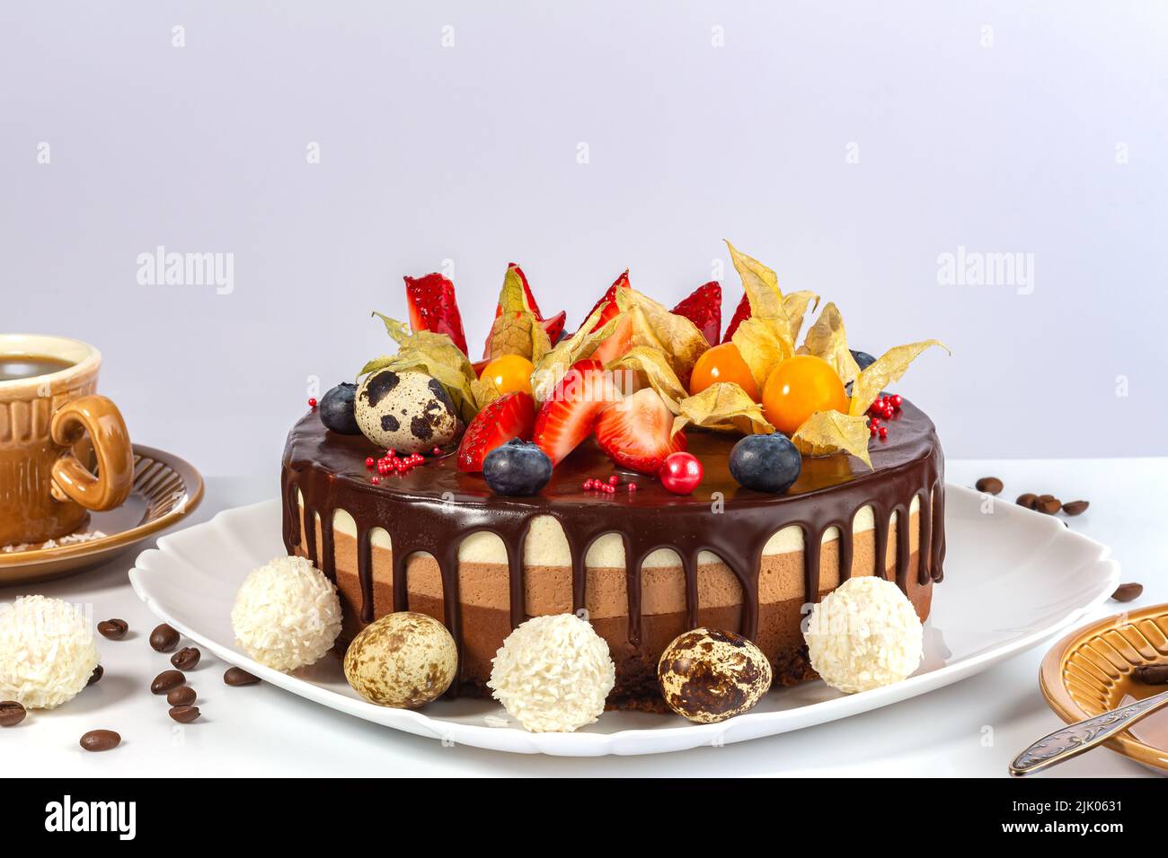 Schokoladenkuchen mit Erdbeeren, Moor Wortleberry, Physalis und Ostern Quai Eier auf grauem Hintergrund. Kuchen drei Schokolade auf weißem Teller mit Tasse Stockfoto