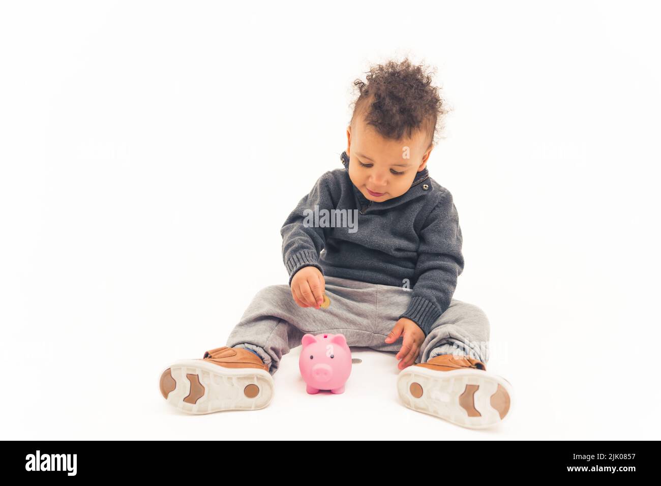 Schönes afroamerikanisches Kind, das eine Münze in ein Sparschwein legt - isoliert. Hochwertige Fotos Stockfoto