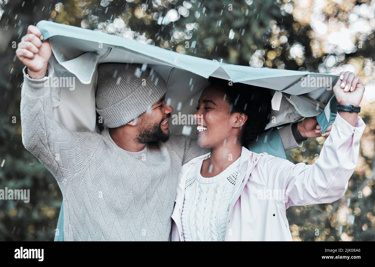 Nicht einmal der Regen kann mich von Euch fernhalten. Ein junges Paar, das draußen im Regen eine Jacke über ihren Köpfen hält. Stockfoto