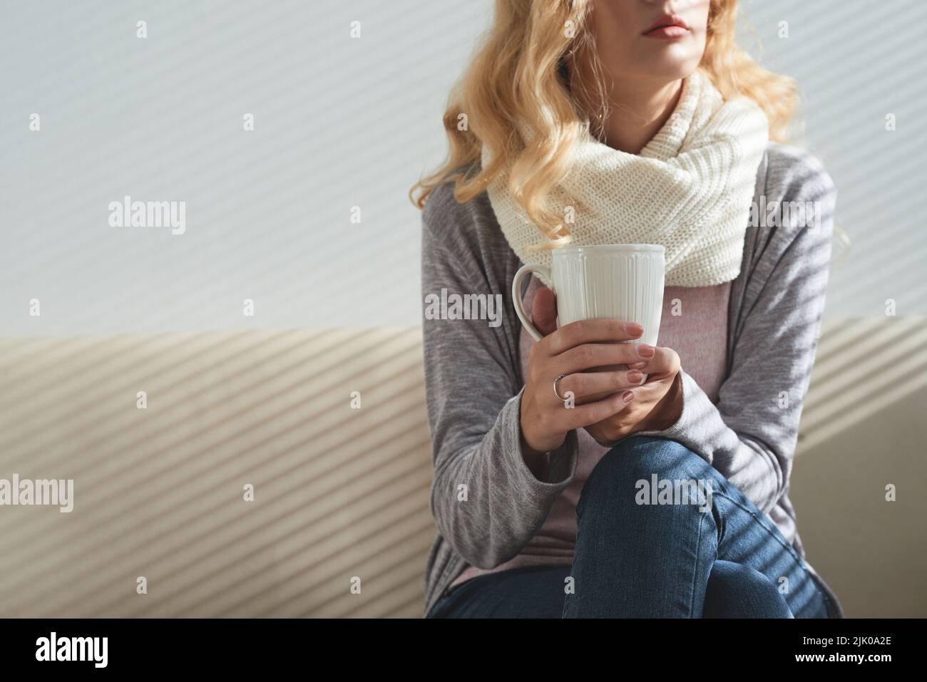 Nachdenkliche junge Frau in warmen Kleidern, die zu Hause Kaffee trinkt Stockfoto