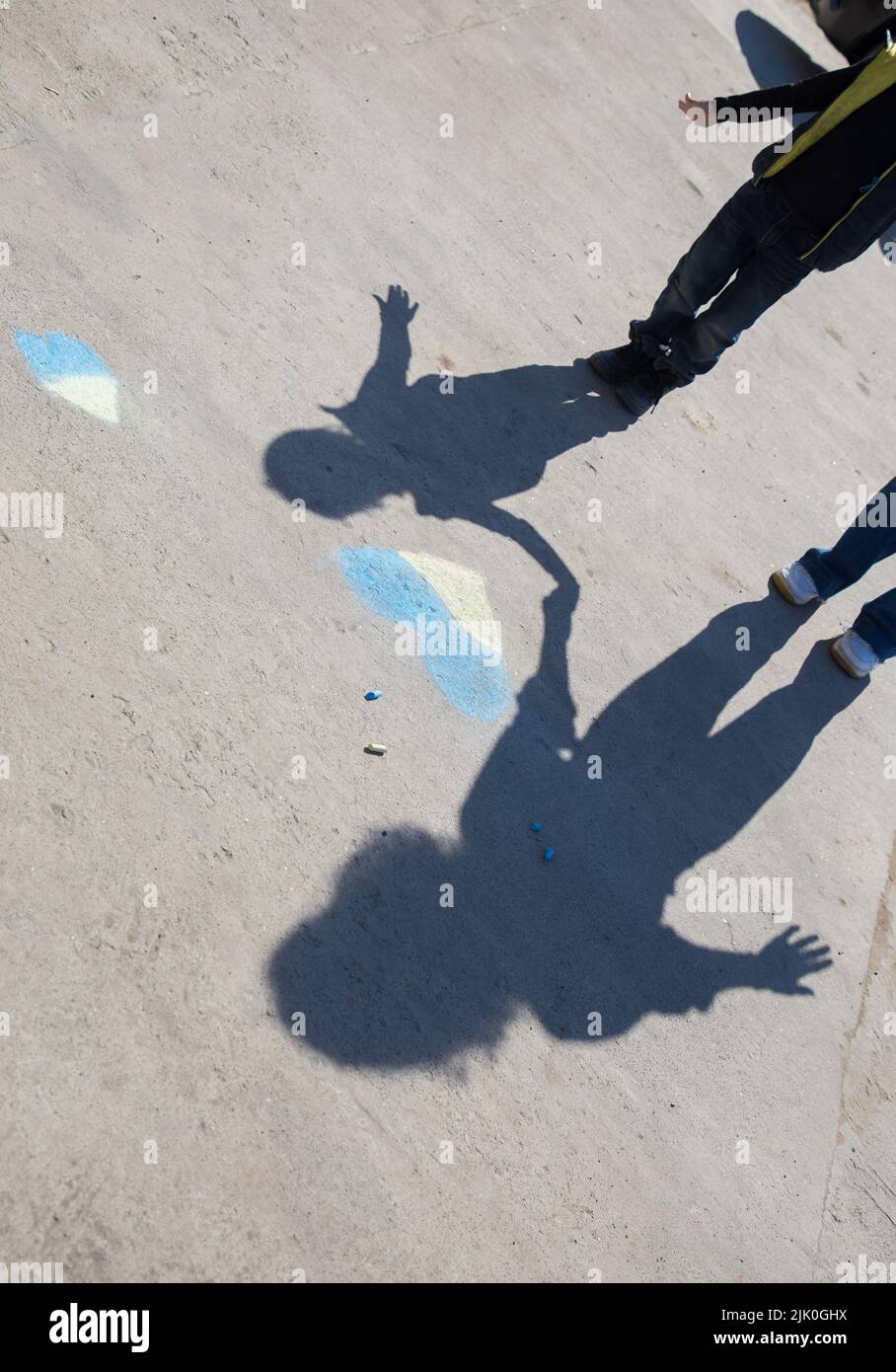 Kontrastierende Schatten auf dem Bürgersteig von zwei Personen, Frau und Kind in der Nähe von gelb-blauem Herz in Buntstiften gezeichnet. Die Ukrainer wollen Frieden. Kindheit während des Krieges in Stockfoto