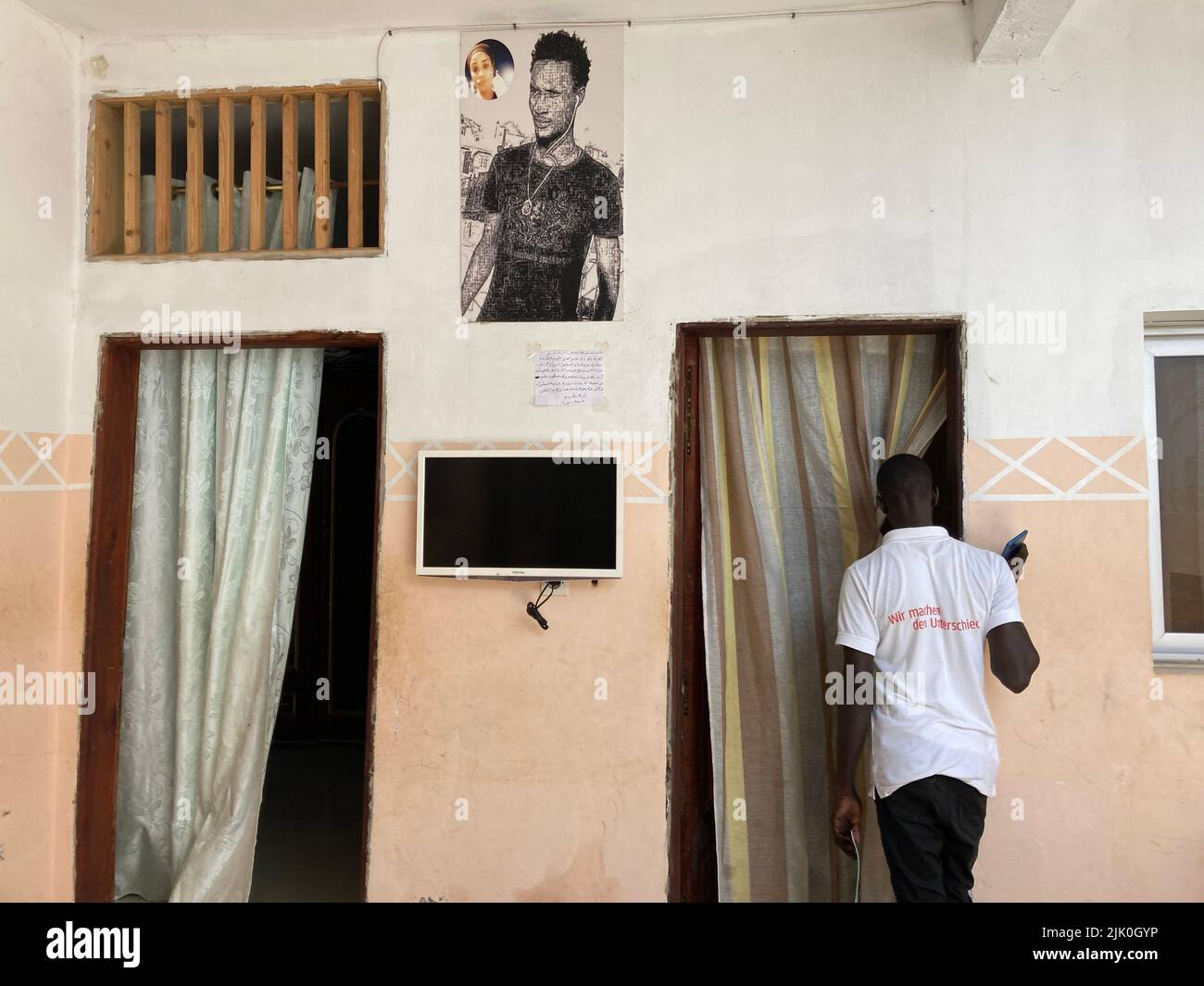 PRODUKTION - 21. Juli 2022, Senegal, Dakar: Abdoulaye Wade, fotografiert in seinem Haus am Stadtrand, geht an einem Bild seines Bruders Cheikh Wade vorbei. Wade wurde letztes Jahr bei Demonstrationen getötet. Senegal gilt als Stabilitätsanker für die krisengeschüttelte Sahelregion, in der auch die deutschen Streitkräfte aktiv sind. Bundeskanzler Scholz besuchte Senegal als erstes Land auf seiner Afrikareise, weil Erdgas bald nach Europa fließen wird. Aber in Westafrikas Vorzeigedemokratie brodelt es über. (An dpa 'Deutschlands neuer Partner Senegal: Demokratie unter Druck') Phot Stockfoto