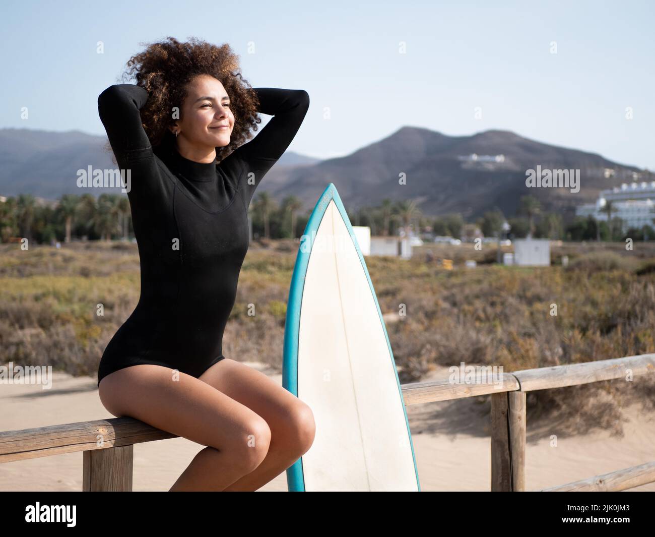 Surfermädchen mit Afro-Haaren auf einem Zaun sitzen Stockfoto