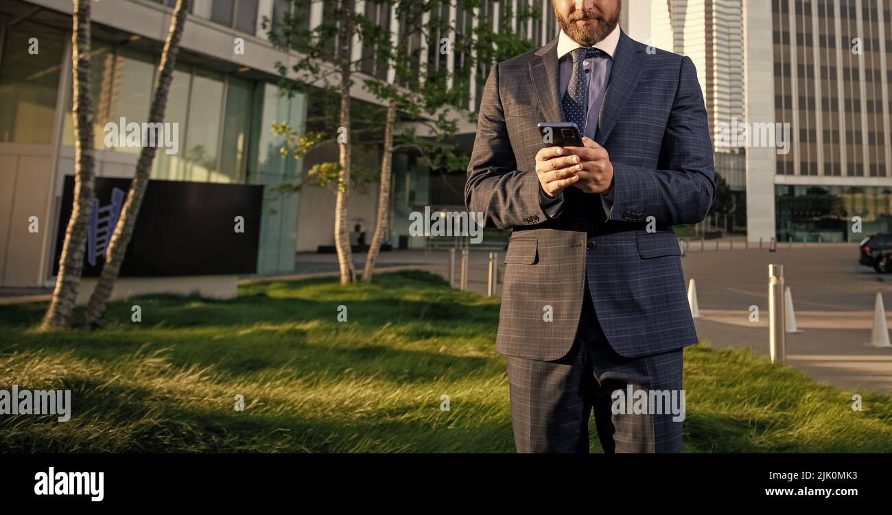 Der kurzgestellte Geschäftsmann im Anzug chattet auf dem Smartphone außerhalb des Büros, verhandelt Stockfoto