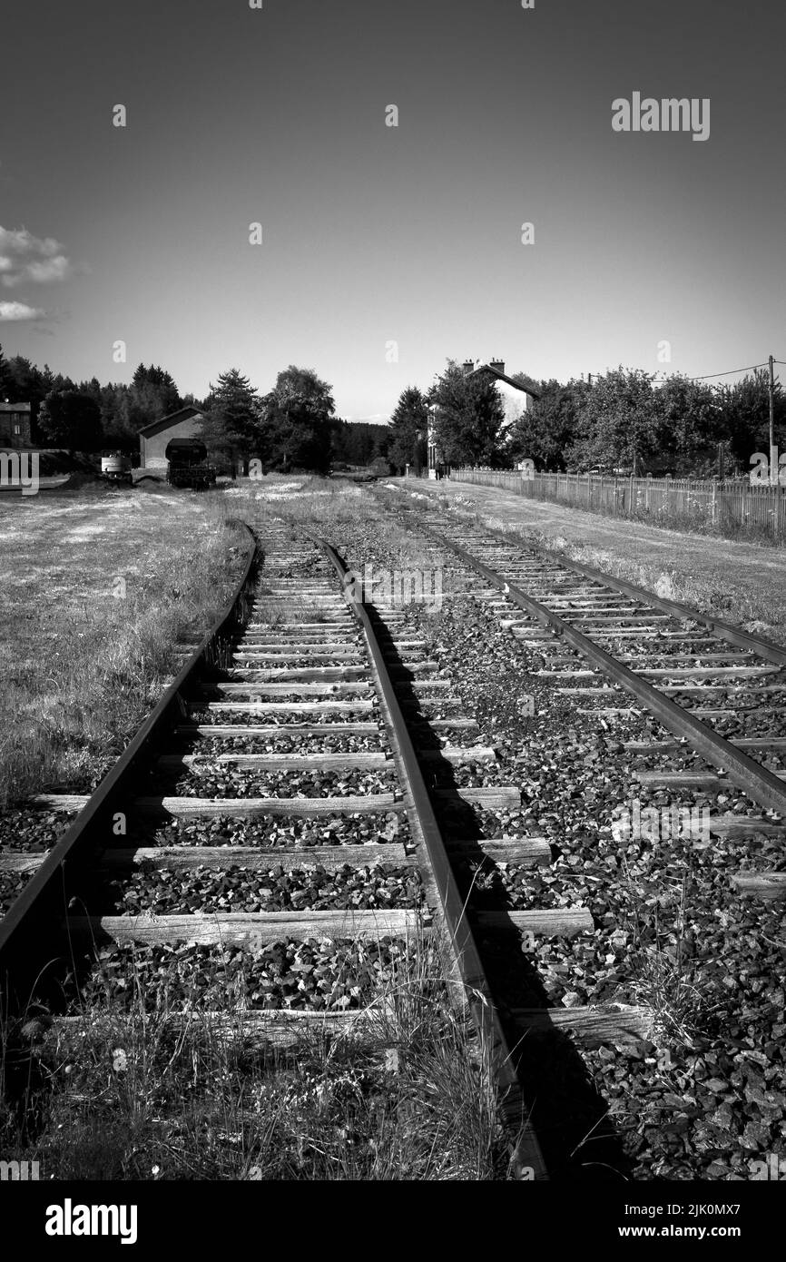 Schwarz-weiß-Ansicht stillgelegter Bahngleise in einem ländlichen Gebiet unter klarem Himmel. Auvergne Rhone Alpes. Frankreich Stockfoto