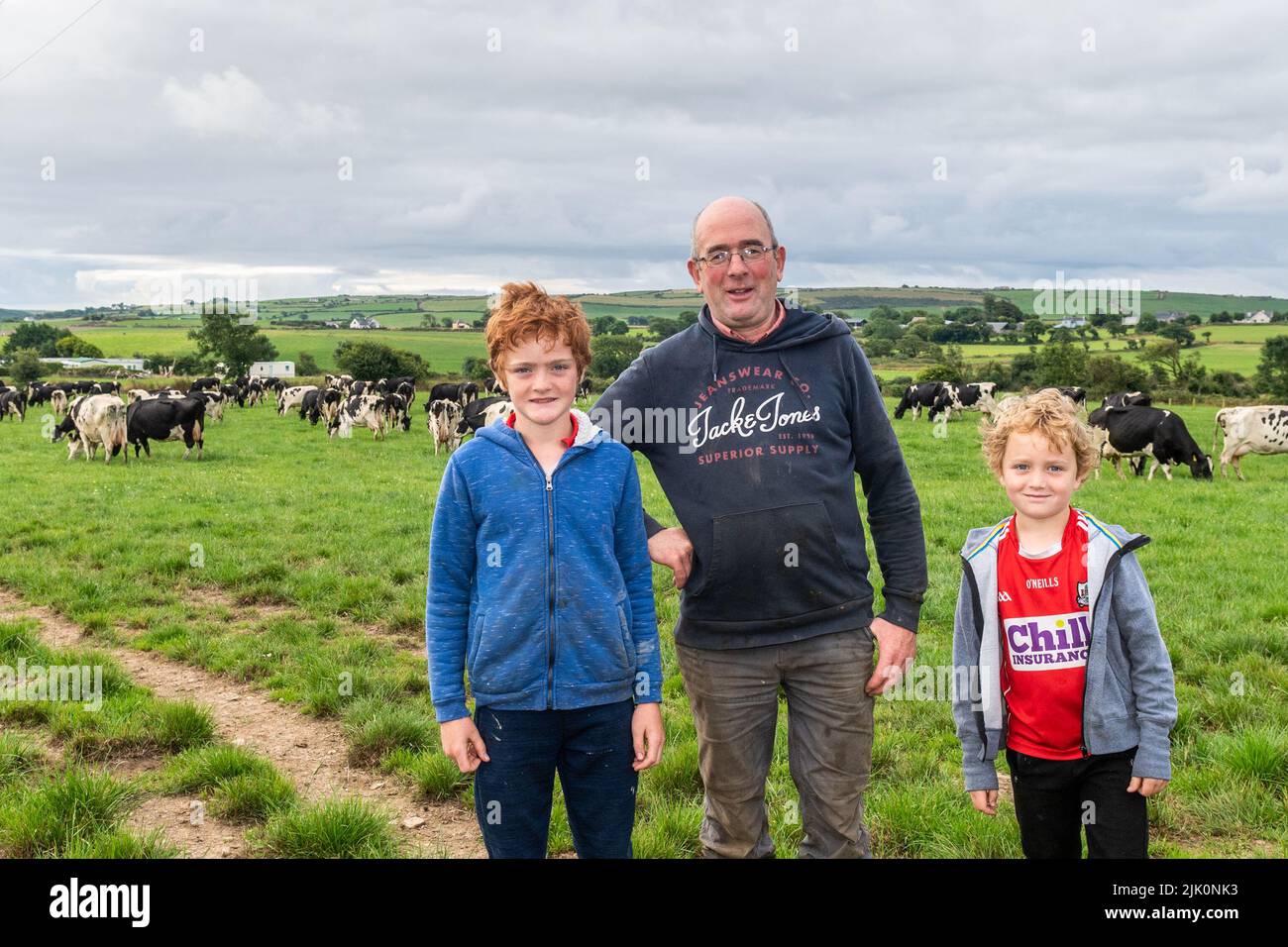 Timoleague, West Cork, Irland. 29.. Juli 2022. Milchbauer DJ Keohane überquert seine Herde Milchkühe über die R600 in der Nähe von Timoleague, nachdem er melkt hatte, wobei einer seiner Söhne, Daniel, mithalf. Die Regierung hat sich gestern Abend auf eine Reduzierung der Emmissionen um 25 % für den Agrarsektor geeinigt. DJ melkt 166 Kühe auf 200 Hektar Land, er ist mit seinen beiden Söhnen Daniel und James abgebildet. Quelle: AG News/Alamy Live News Stockfoto