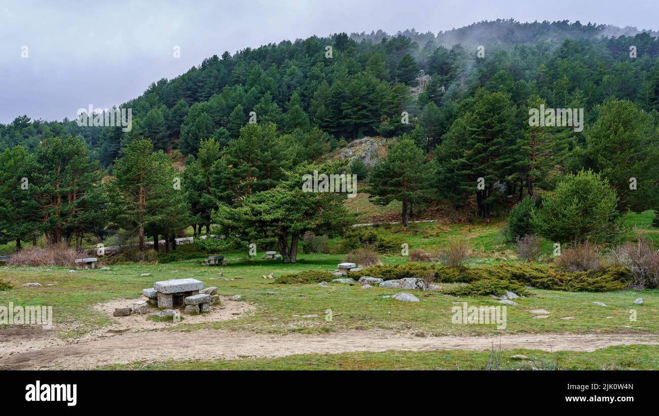 Steintisch und Sitzplätze zum Essen in der Hochgebirgslandschaft an einem bewölkten Tag. Canencia Madrid. Stockfoto