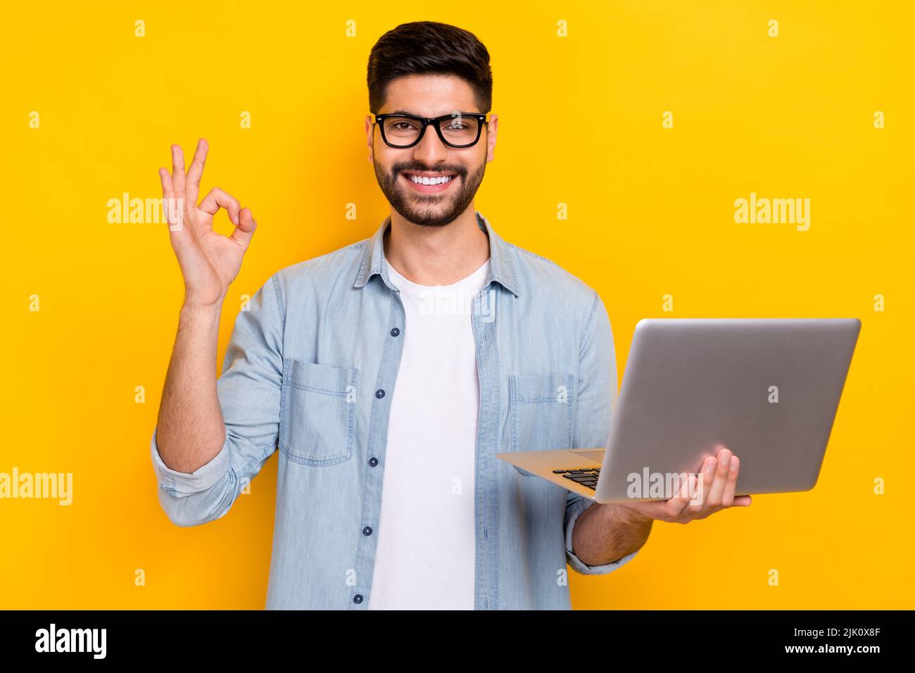 Foto von jungen Business guy hält Laptop zeigt okey Zeichen kaufen Werbung google glücklich isoliert auf gelbem Hintergrund Stockfoto