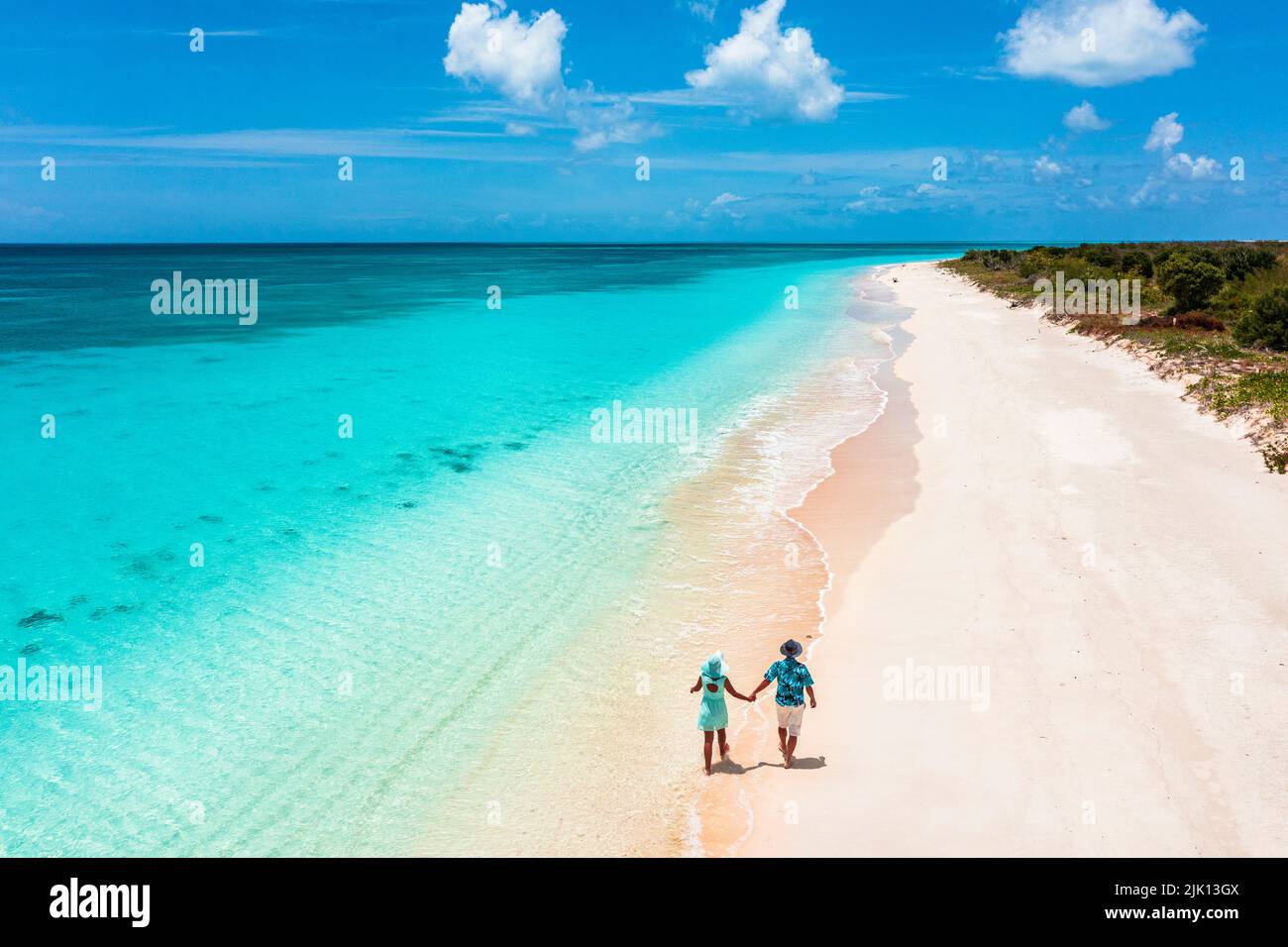 Mann und Frau gehen Hand in Hand an einem Strand, der vom türkisfarbenen Meer gewaschen wird, Barbuda, Antigua und Barbuda, Westindien, Karibik, Mittelamerika Stockfoto