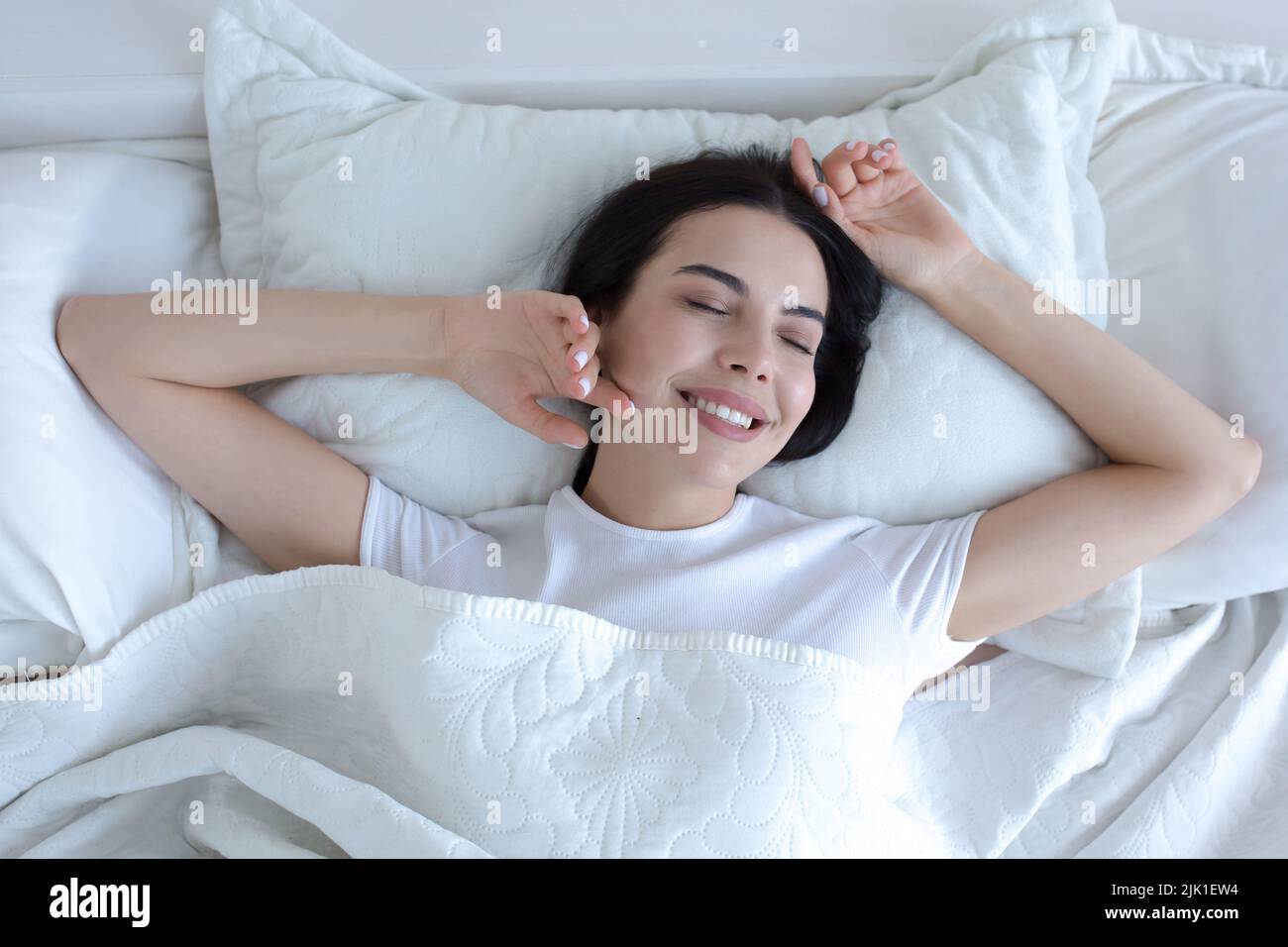 Draufsicht, junge schöne Brünette Frau schlafen im Bett mit geschlossenen Augen, lächelnd im Schlaf tragen weißen T-Shirt Pyjamas Stockfoto
