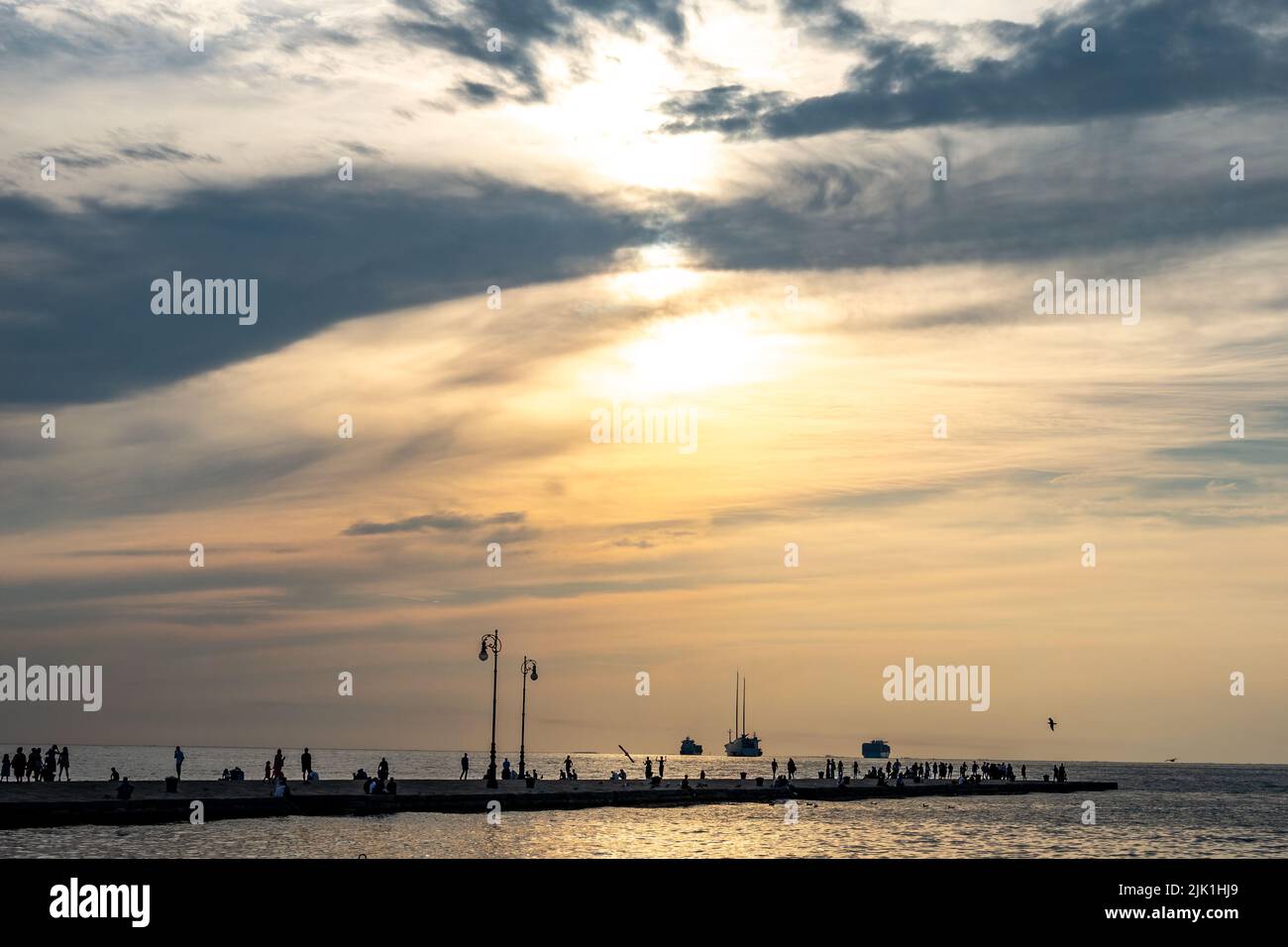 Triest, Italien, 28. Juli 2022. Die Menschen genießen den Sonnenuntergang am Molo Audace (Audace Pier) vor der größten Segelyacht der Welt (C) und zwei Crui Stockfoto