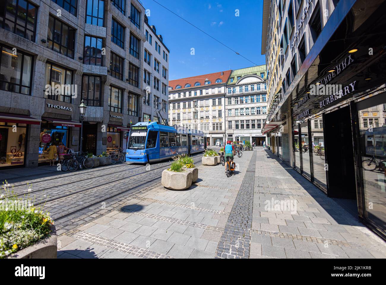 München, 6. Juli 2022: Entlang der Perusastraße, Erweiterung der Maximilianstraße mit nicht weniger teuren Geschäften. Eine blaue Straßenbahn fährt durch die Buschstraße Stockfoto