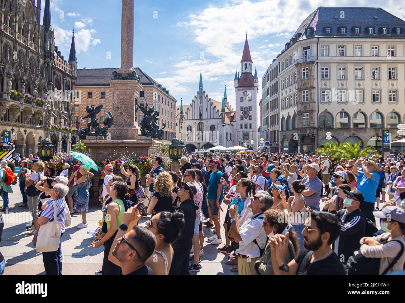 München, 6. Juli 2022: Touristen am Marienplatz staunen über das Glockenspiel auf dem Neuen Rathaus. Blick über die Köpfe der Besucher bis zum Stockfoto