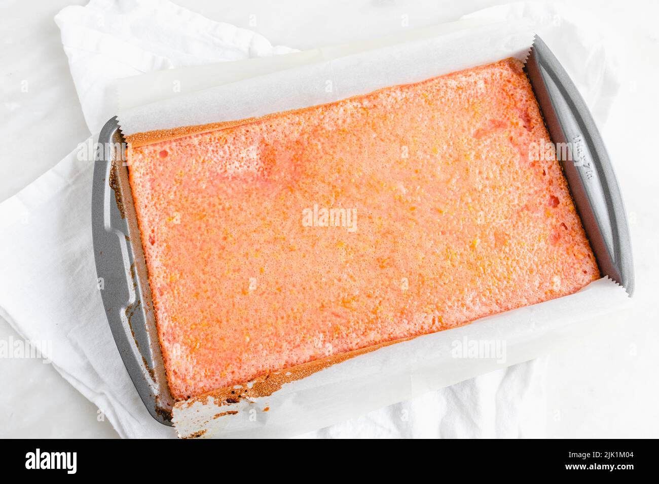 Overhead-Ansicht von Pink Grapefruit Dessertbars in einer Backform: Frisch gebackenes Gebäck in einer mit Pergamentpapier ausgekleideten Metallpfanne Stockfoto