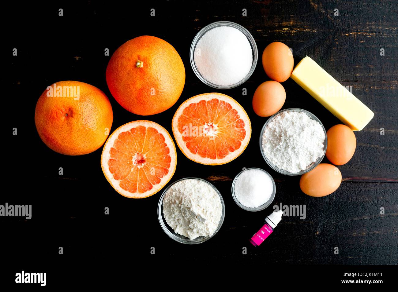 Pink Grapefruit Dessert Bar Zutaten auf einem Holztisch: Rote Grapefruit, Mehl, Zucker, weitere Zutaten auf dunklem Hintergrund Stockfoto
